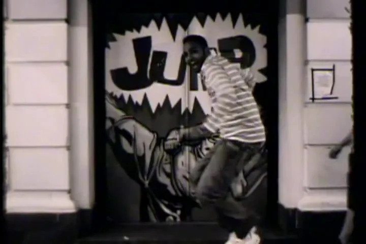 A frame from Just Do It!, in black and white: a man in a striped shirt caught mid-stride in front of a painted shutter